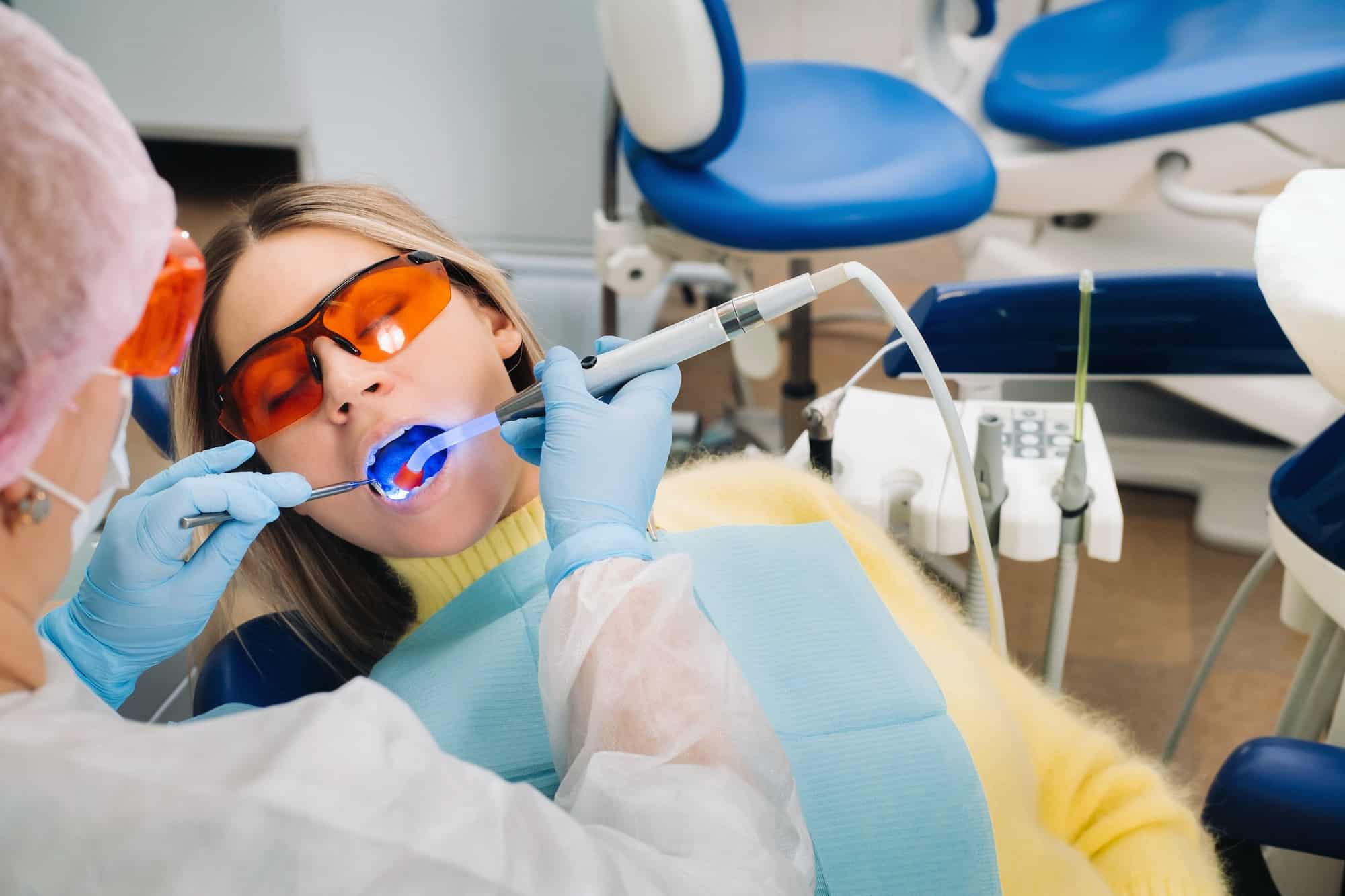 A young beautiful girl in dental glasses treats her teeth at the dentist with ultraviolet light