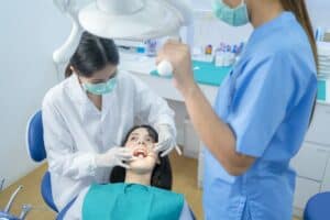 Asian female dentist checking or examining tooth of young girl patient lying on dental chair.