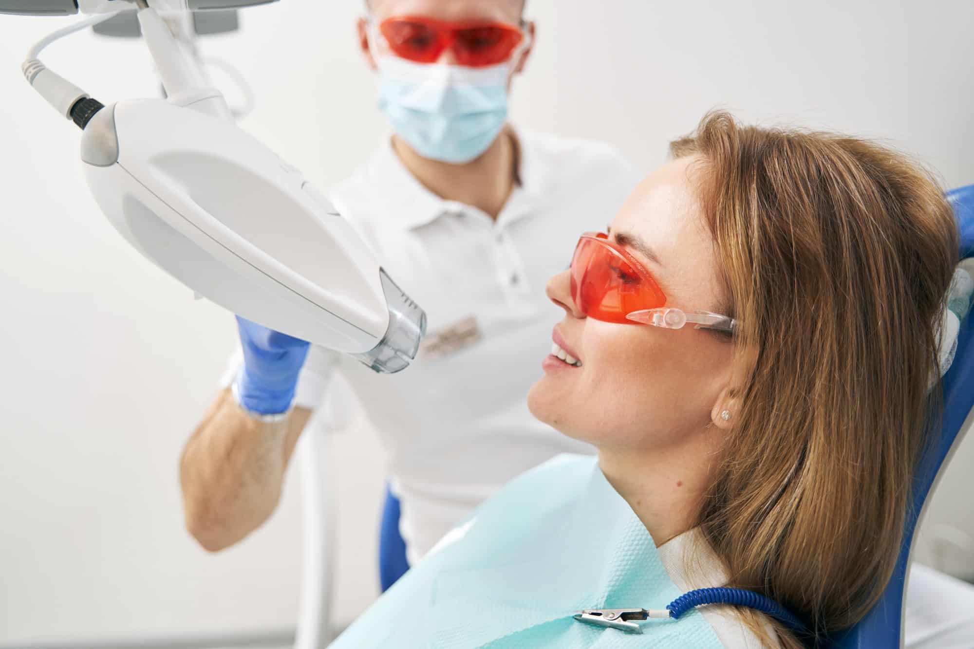 Woman having laser teeth whitening procedure in dental clinic